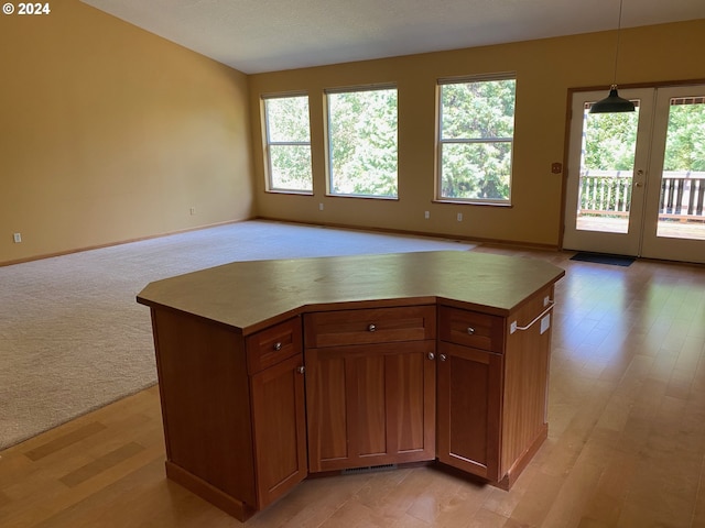 kitchen featuring light carpet, baseboards, open floor plan, brown cabinets, and hanging light fixtures