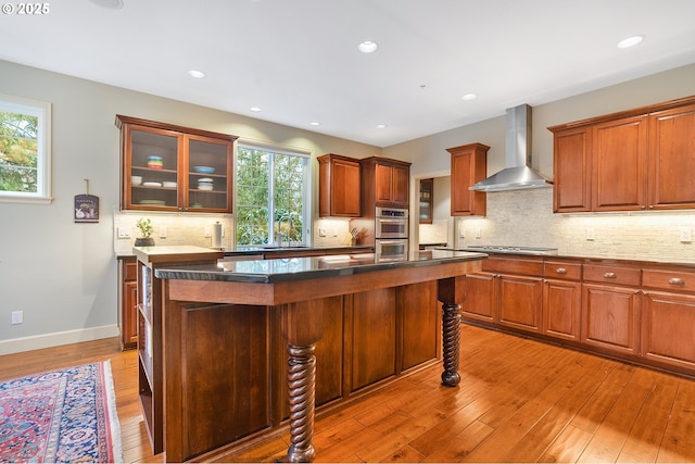 kitchen featuring light hardwood / wood-style floors, stainless steel appliances, a kitchen island, wall chimney range hood, and tasteful backsplash