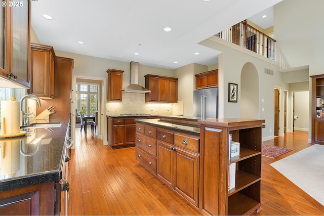 kitchen with sink, high quality fridge, light hardwood / wood-style flooring, a kitchen island, and wall chimney range hood