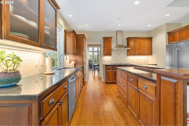 kitchen with sink, stainless steel appliances, light wood-type flooring, tasteful backsplash, and wall chimney range hood