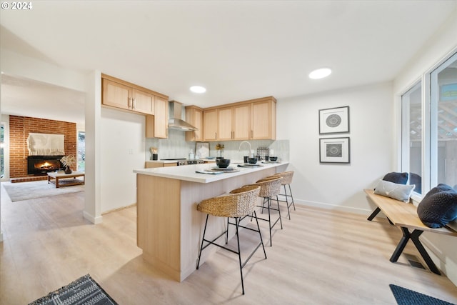 kitchen with light brown cabinetry, a kitchen breakfast bar, kitchen peninsula, light wood-type flooring, and wall chimney exhaust hood