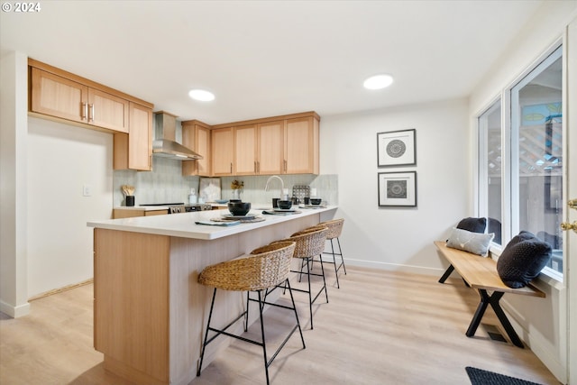 kitchen featuring tasteful backsplash, a breakfast bar, wall chimney range hood, and light brown cabinets