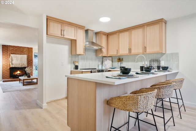 kitchen with a kitchen breakfast bar, wall chimney range hood, and light brown cabinets