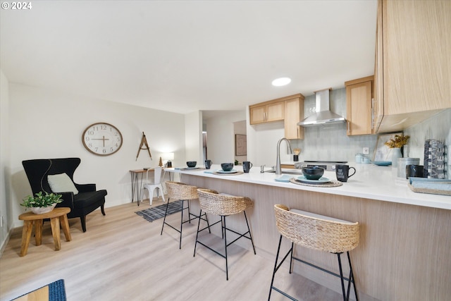 kitchen with backsplash, a kitchen bar, light brown cabinetry, kitchen peninsula, and wall chimney exhaust hood