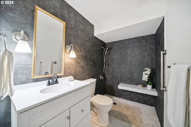 bathroom with tiled shower, vanity, toilet, and tile walls