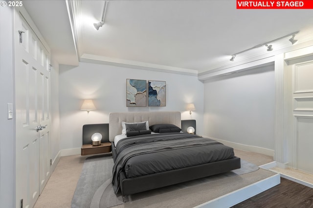 carpeted bedroom featuring a closet, baseboards, crown molding, and track lighting