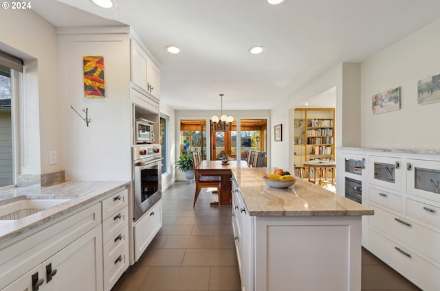 kitchen with light stone counters, a kitchen island, decorative light fixtures, white cabinetry, and stainless steel appliances