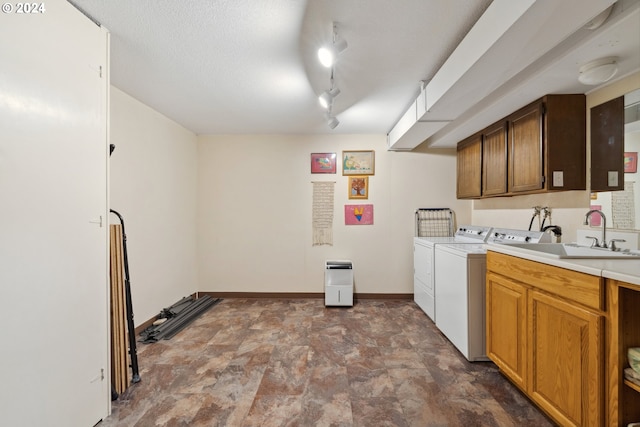 washroom featuring sink, washing machine and clothes dryer, a textured ceiling, track lighting, and cabinets