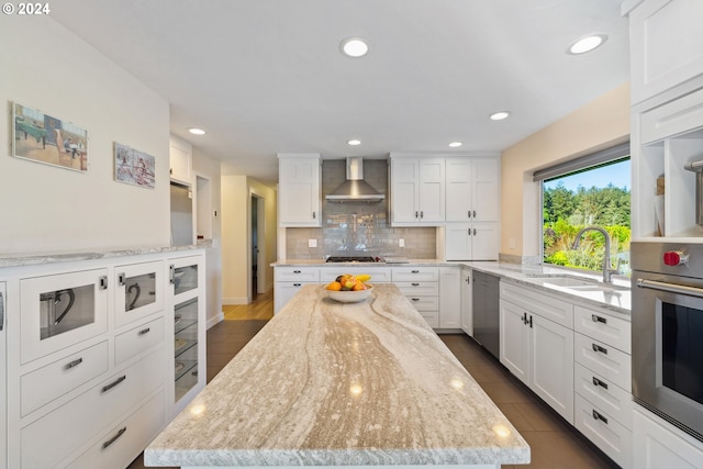 kitchen with appliances with stainless steel finishes, wall chimney exhaust hood, white cabinetry, and sink