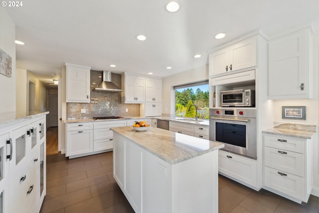 kitchen featuring white cabinetry, light stone counters, stainless steel appliances, sink, and wall chimney range hood