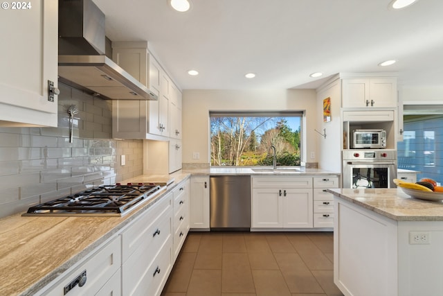 kitchen featuring appliances with stainless steel finishes, white cabinetry, sink, and wall chimney range hood