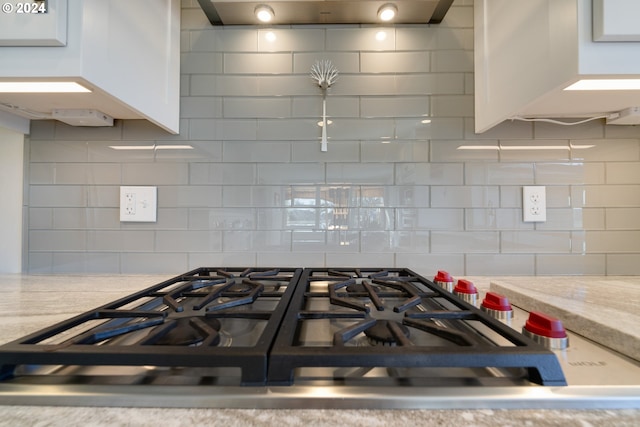 kitchen featuring light stone counters, stainless steel stovetop, white cabinetry, and decorative backsplash