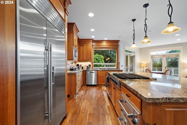 kitchen featuring a center island, built in appliances, decorative light fixtures, and dark stone countertops