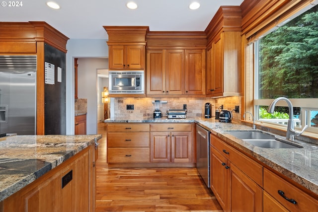 kitchen featuring a healthy amount of sunlight, built in appliances, sink, and light hardwood / wood-style flooring