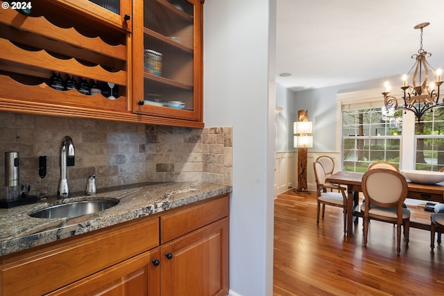 kitchen with sink, an inviting chandelier, hardwood / wood-style flooring, stone counters, and pendant lighting