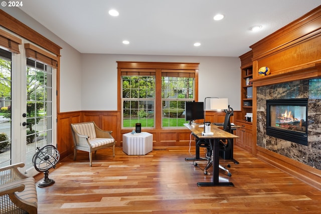 home office with a high end fireplace, a wealth of natural light, light wood-type flooring, and built in shelves