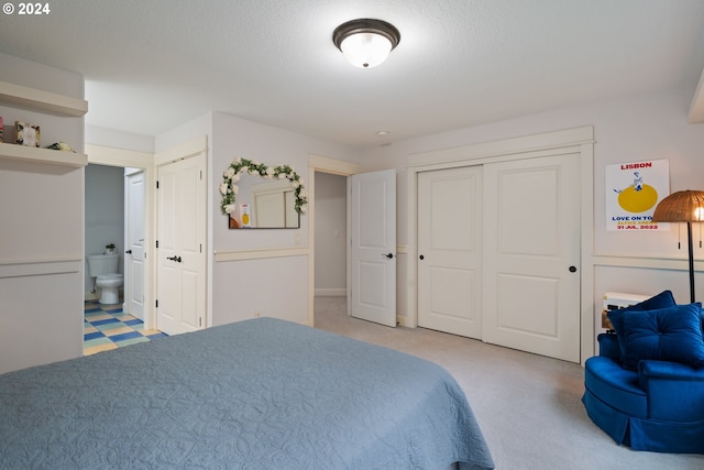 bedroom featuring light carpet, ensuite bath, and a textured ceiling