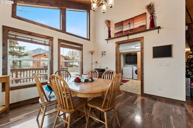 dining space with washing machine and clothes dryer, wood-type flooring, a towering ceiling, and an inviting chandelier