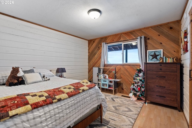 bedroom with wood walls, light hardwood / wood-style floors, and a textured ceiling