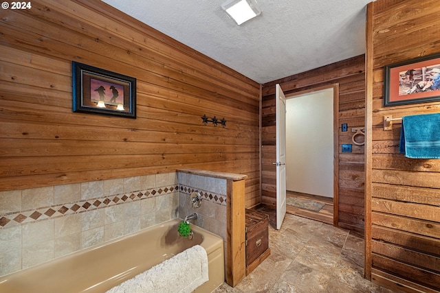 bathroom featuring a tub to relax in, wooden walls, and a textured ceiling