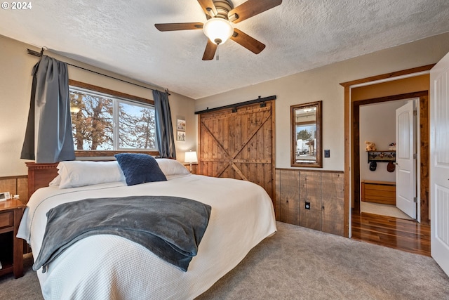 carpeted bedroom with a barn door, wooden walls, ceiling fan, and a textured ceiling