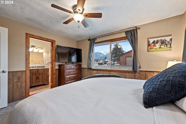 bedroom with ceiling fan, ensuite bathroom, light colored carpet, a textured ceiling, and wooden walls