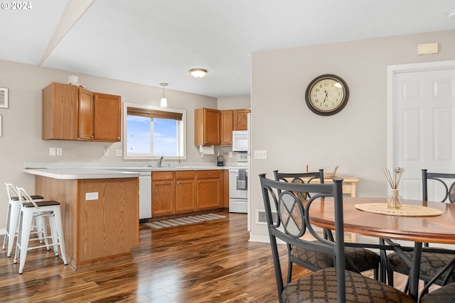 kitchen with white appliances, sink, kitchen peninsula, dark wood-type flooring, and a breakfast bar