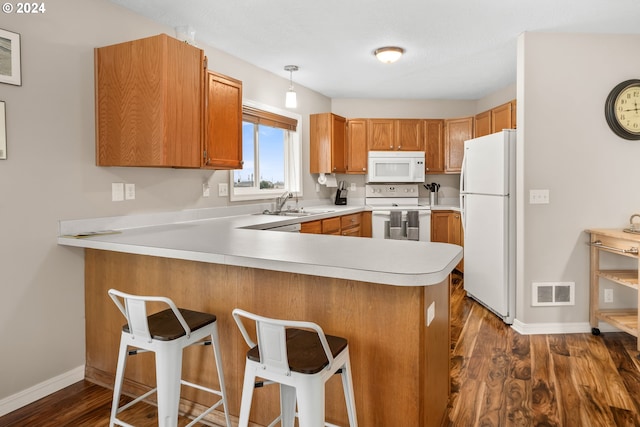 kitchen with kitchen peninsula, pendant lighting, dark wood-type flooring, white appliances, and a kitchen bar