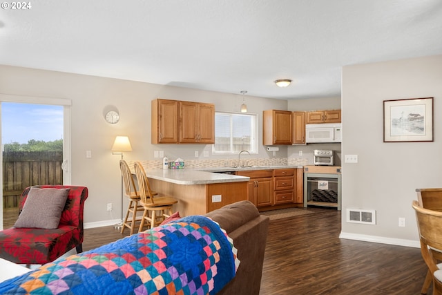 kitchen featuring kitchen peninsula, hanging light fixtures, sink, a breakfast bar, and dark hardwood / wood-style floors