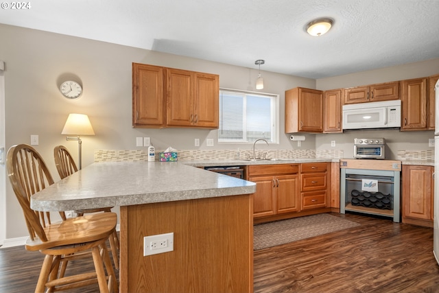 kitchen with kitchen peninsula, pendant lighting, dark hardwood / wood-style flooring, sink, and a kitchen bar