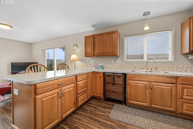 kitchen featuring kitchen peninsula, pendant lighting, dishwashing machine, sink, and dark hardwood / wood-style floors