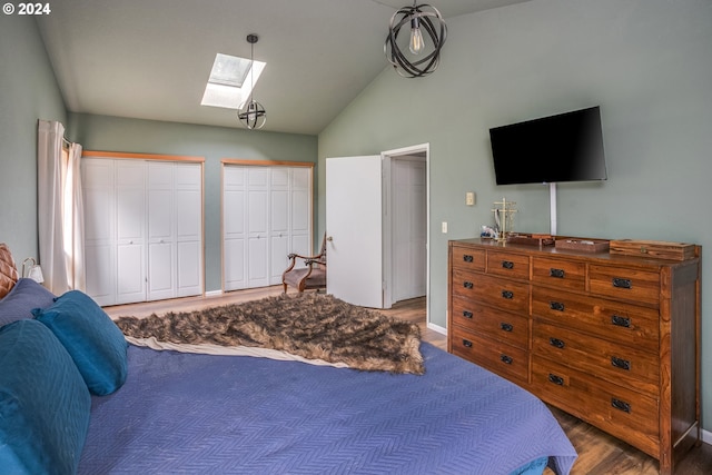 bedroom with lofted ceiling with skylight, baseboards, two closets, and wood finished floors