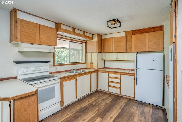 kitchen with a textured ceiling, under cabinet range hood, white appliances, a sink, and dark wood finished floors