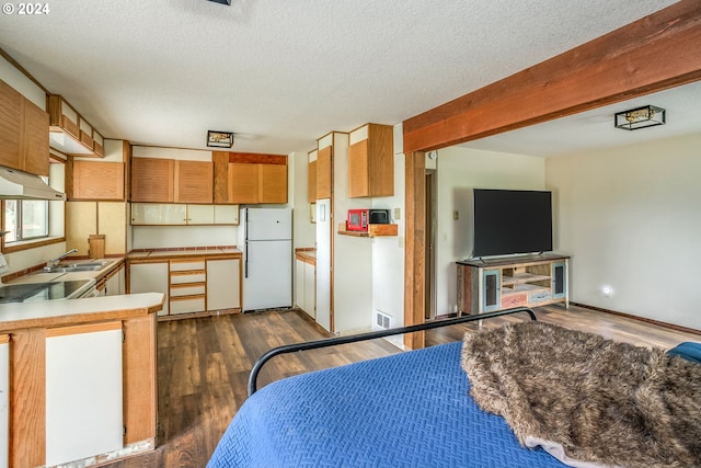 bedroom with a textured ceiling, beamed ceiling, dark wood finished floors, and freestanding refrigerator