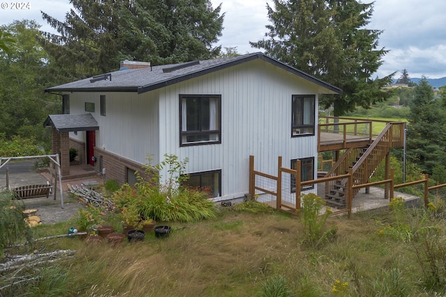 back of property with stairs, roof with shingles, and a wooden deck