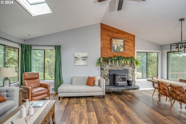 living area with a wood stove, lofted ceiling with skylight, a ceiling fan, and wood finished floors