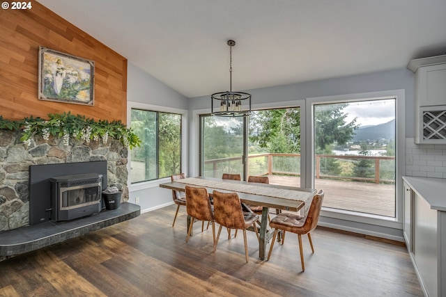 dining space with baseboards, wood finished floors, a wood stove, vaulted ceiling, and a chandelier