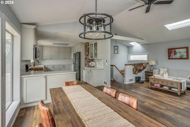 dining space featuring lofted ceiling with skylight, dark wood-style flooring, visible vents, and ceiling fan