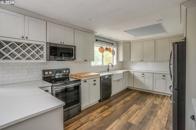 kitchen featuring dark wood finished floors, backsplash, light stone countertops, stainless steel appliances, and a sink