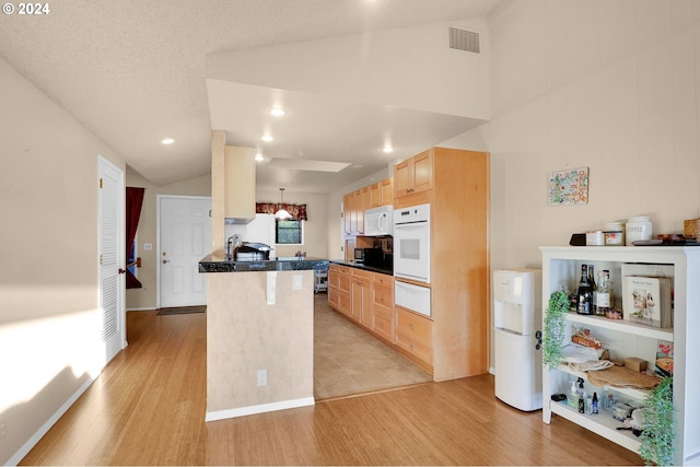 kitchen featuring light brown cabinets, light hardwood / wood-style flooring, kitchen peninsula, vaulted ceiling, and white appliances