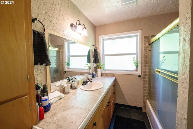 bathroom featuring shower / bath combination with glass door, vanity, and a textured ceiling