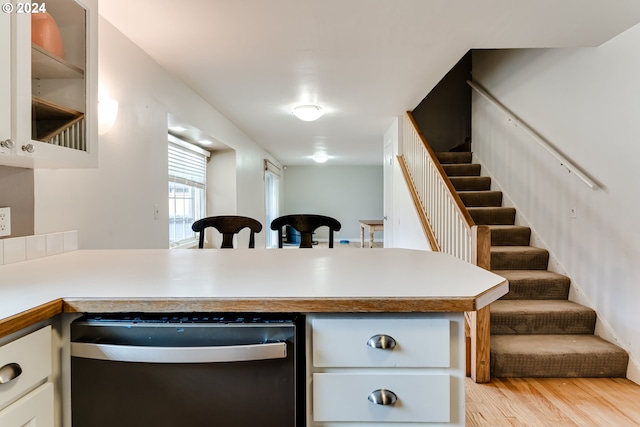 kitchen with stainless steel dishwasher, white cabinets, light wood-type flooring, and kitchen peninsula