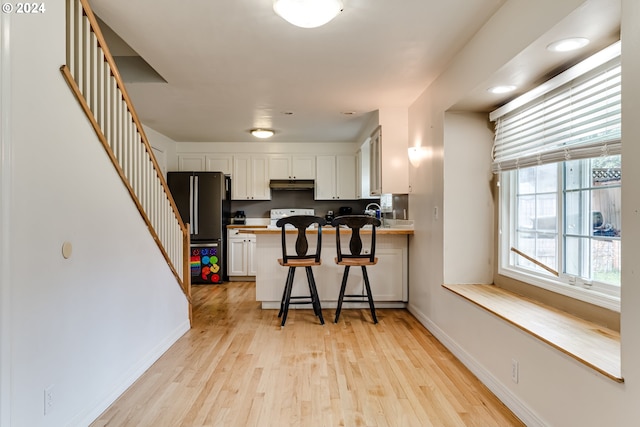 kitchen featuring light hardwood / wood-style floors, kitchen peninsula, a breakfast bar area, white cabinetry, and stainless steel fridge