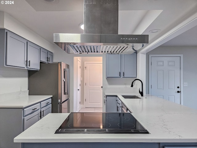 kitchen with black electric stovetop, wall chimney range hood, sink, gray cabinets, and stainless steel refrigerator