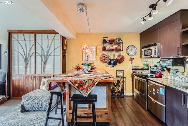 kitchen featuring a breakfast bar, stainless steel appliances, rail lighting, dark wood-type flooring, and baseboards