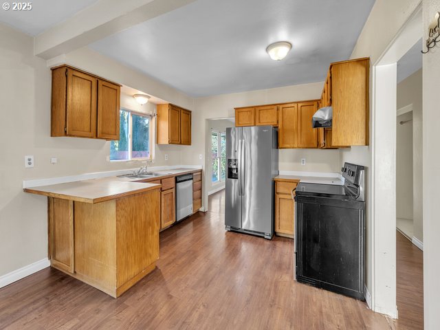 kitchen with ventilation hood, hardwood / wood-style flooring, kitchen peninsula, and appliances with stainless steel finishes