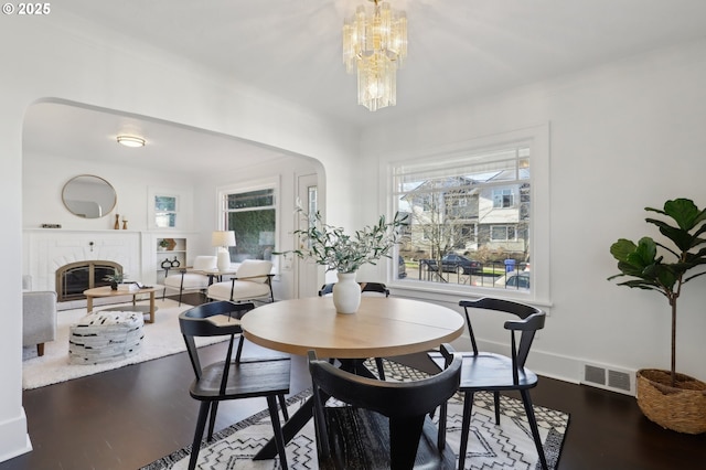 dining space with a fireplace, wood-type flooring, a wealth of natural light, and a notable chandelier