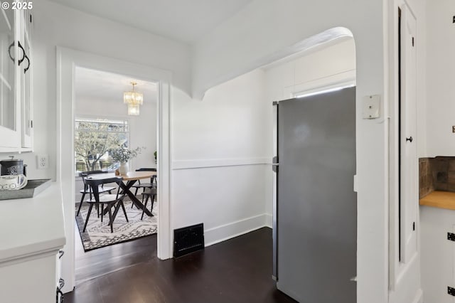 interior space with stainless steel fridge, white cabinets, a chandelier, and dark hardwood / wood-style floors