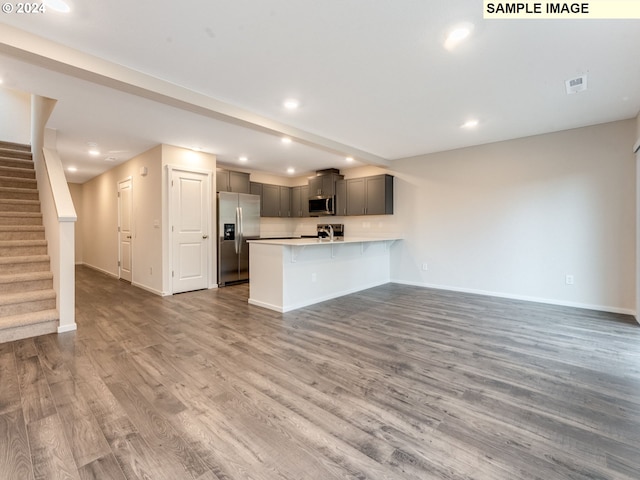 kitchen featuring kitchen peninsula, appliances with stainless steel finishes, gray cabinetry, a breakfast bar, and hardwood / wood-style floors