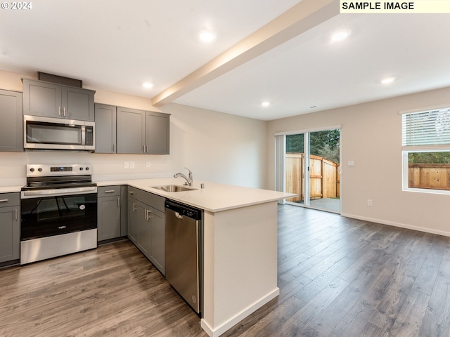 kitchen with kitchen peninsula, gray cabinetry, stainless steel appliances, dark wood-type flooring, and sink